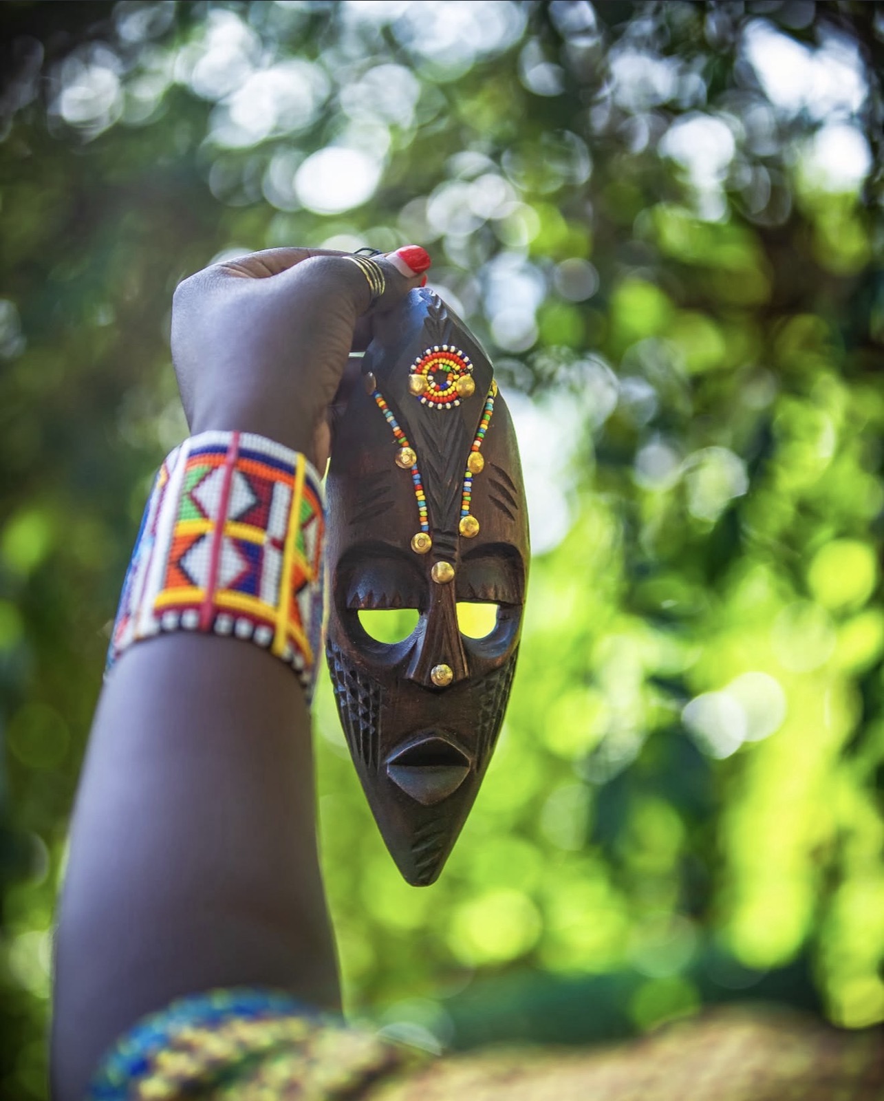 Beaded wrist holding a carved mask against the greenery